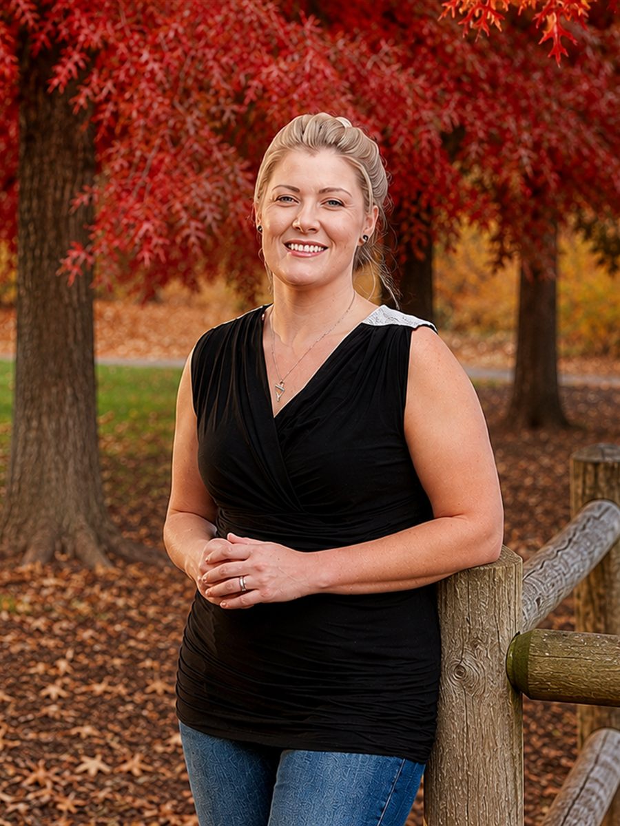 Chelsey Smits of Heritage Funeral and Cremation, standing at a rail fence beneath red autumn trees in Spokane